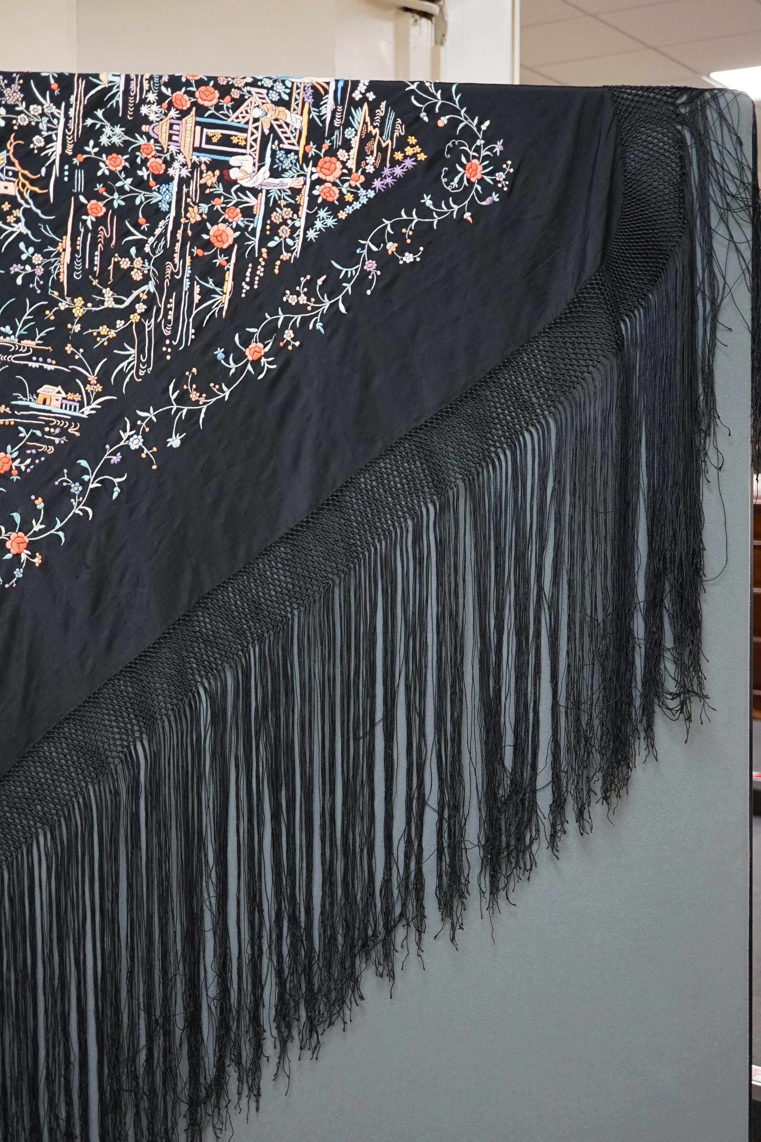 An early 20th century Chinese black silk shawl, with all over coloured floral embroidery, embroidered with multi-coloured silks and a long silk fringe, unusually the four corners are embroidered with a figurative pagoda